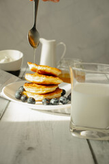 Cottage cheese pancakes with blueberries and sour cream on a white wooden table