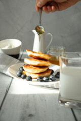 Cottage cheese pancakes with blueberries and sour cream on a white wooden table