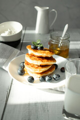 Cottage cheese pancakes with blueberries and sour cream on a white wooden table