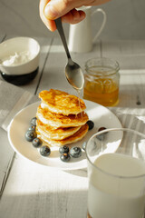 Cottage cheese pancakes with blueberries and sour cream on a white wooden table