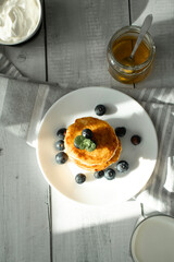 Cottage cheese pancakes with blueberries and sour cream on a white wooden table
