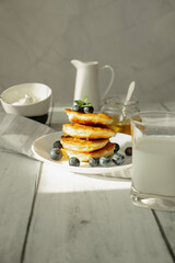 Cottage cheese pancakes with blueberries and sour cream on a white wooden table