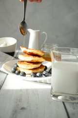 Cottage cheese pancakes with blueberries and sour cream on a white wooden table