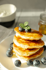 Cottage cheese pancakes with blueberries and sour cream on a white wooden table