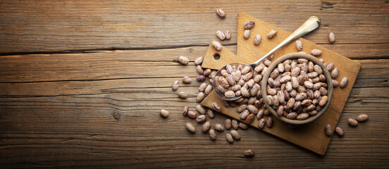 Dried pinto beans in wooden bowl with cutting board and spoon on old wooden background, close-up, space for text.