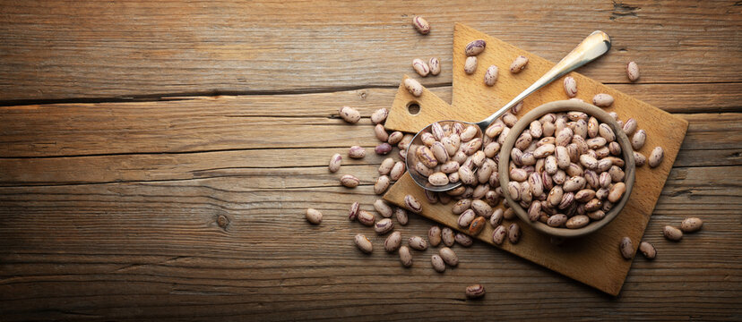 Dried pinto beans in wooden bowl with cutting board and spoon on old wooden background, close-up, space for text.