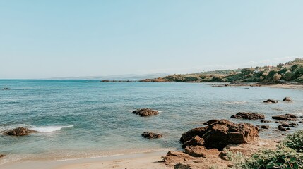 Serene coastal landscape; tranquil beach, clear water, rocks, distant hills; ideal for travel brochures