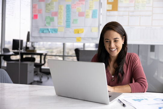 Successful and inspired. Smiling motivated millennial businesswoman project manager finance analyst scrum master engaged in professional development at workplace watch webinar on notebook. Copy space