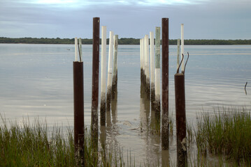 Posts standing on the shore of Cananeia channel early morning at sunrise. Calm waters, clear sky, sunny day