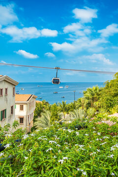 Fototapeta Tropical coastal view with flowering plants, seaside buildings and a cable car gondola moving over the ocean on Phu Quoc island, Vietnam at Sunset town with Mediterranean style architecture