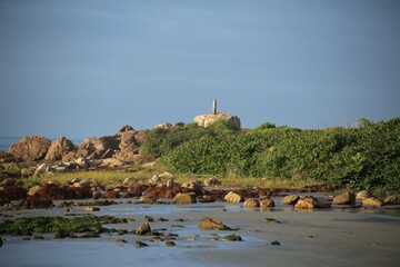 Rocks spread out on the beach sand, hill covered by green vegetation, sunny day light, clear sky. Wastern side of  Itacuruca beach, Cananeia, Sao Paulo state
