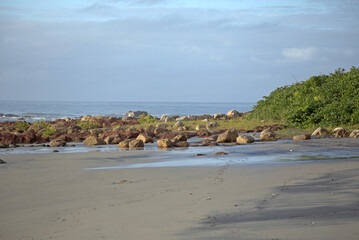 Itacuruca beach, Cananeia, south Sao Paulo state, rocks spread out on beach sand, green vegtaion, clear blue sky, sunny day morning