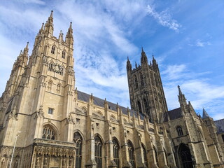 Naklejka premium Majestic Canterbury Cathedral towers reaching towards a bright blue sky with dynamic clouds