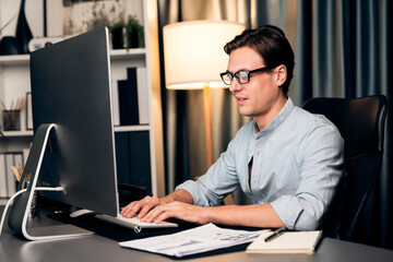 Smart businessman analyzing business paragraph dynamic database marketing analysis plan surrounded paper sheet and pc monitor report to compare with document data at home office at night. Pecuniary.