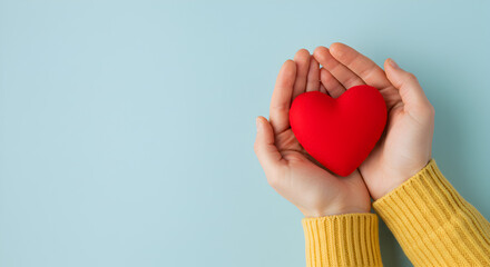 Obraz premium Red Heart Held Lovingly in Hands with a Yellow Sweater Sleeve on a Light Blue Background