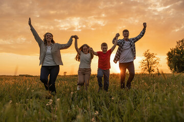 A joyful family celebrates together with arms raised against a stunning sunset backdrop in a...