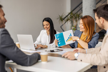 Businesswoman sitting at corporate office with chart in hands and analyzing data with her team of experts.