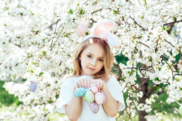 Easter egg hunt. Girl child Wearing Bunny Ears Running To Pick Up Egg In Garden. Easter tradition. Baby with basket full of colorful eggs.