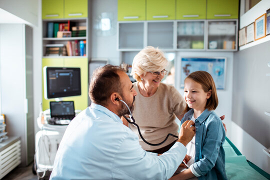 Doctor examining young girl with stethoscope while grandmother watches in medical clinic