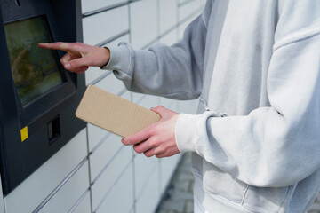 Man placing parcel into outdoor self-service locker touchscreen. Young man uses touchscreen to pick up a cardboard package from a self-service parcel locker