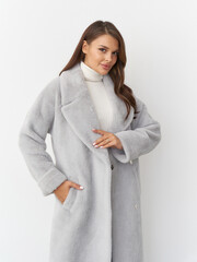 Smiling woman with long brown hair wearing a stylish light gray coat over a white turtleneck...
