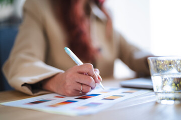 An Arab businesswoman reviews charts with a pen in hand. She is analyzing data for a project.