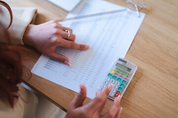 An Arab woman reviews financial data. She is using a calculator to analyze the numbers on the document.