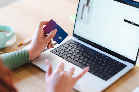 An Arab woman shops online using a laptop and a credit card. She is browsing a fashion website, selecting clothes for purchase. card. She is browsing a Mango website, possibly purchasing a dress.