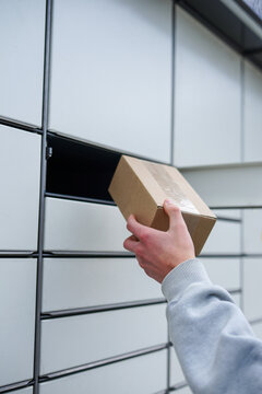 Person using parcel locker to drop off or pick up package. Close-up of a mans hand placing or retrieving a cardboard box from an automated parcel locker