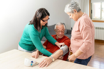 Fototapeta premium Daughter and wife taking blood pressure of smiling senior man with tensiometer at home