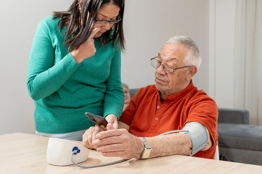 Daughter carefully checking her senior father's blood pressure at home, providing support and care for his health
