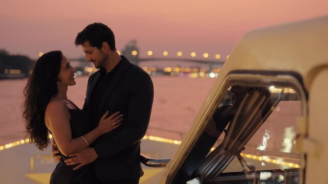 Portrait of affectionate Latin American couple kisses near cockpit on luxury yacht at night. Romantic Hispanic man and woman express passion travelling by motorboat in Thailand