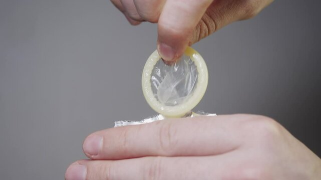 A close-up of a man's hands removing a condom from the packaging before sexual intercourse, on a white background.