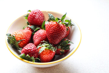 Ripe strawberries in a plate on the kitchen table, close-up
