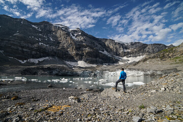 Naklejka premium sporty alpinist stands in front of a glacial lake and looks at the mountains, Klausen Pass, Switzerland