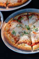 Delicious cheese pizza served on a metal tray with fresh herbs in an outdoor setting during a sunny day