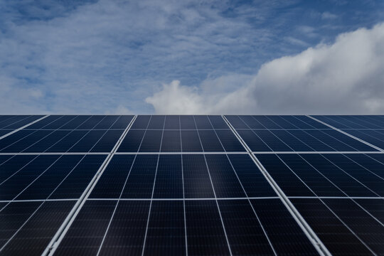 Blue solar panels close up with dark blue and cloudy skies above as sign of changing and challenging times in green energy sector changing prices during cloudy weather