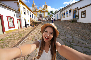 Tourist girl takes self portrait in the historic center of Tiradentes with on background the Mother...