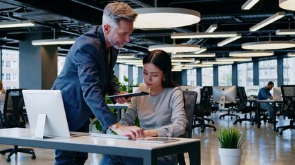 The IT project manager visits a female team member to discuss concepts and review her assignments in their contemporary office setting, where colleagues collaborate as part of a development team in a - Powered by Adobe