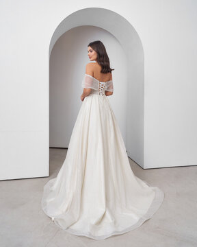 Brunette woman in wedding dress poses gracefully in bright interior with arch