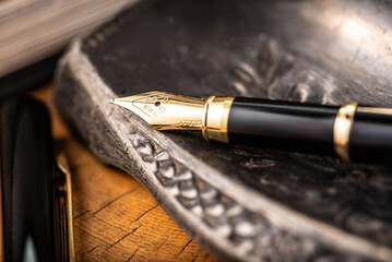 Naklejka premium Fountain pen, a beautiful fountain pen with books and other objects on a rustic wooden surface, selective focus.