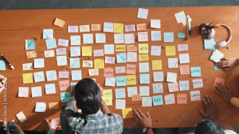 Poster top down view of smart project manager pointing at sticky note on meeting table with sticky notes. s