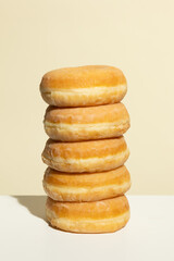 A perfectly stacked tower of five glazed donuts stands against a pastel beige background, showcasing symmetry, texture, and warm tones in a clean and minimal food photography composition.