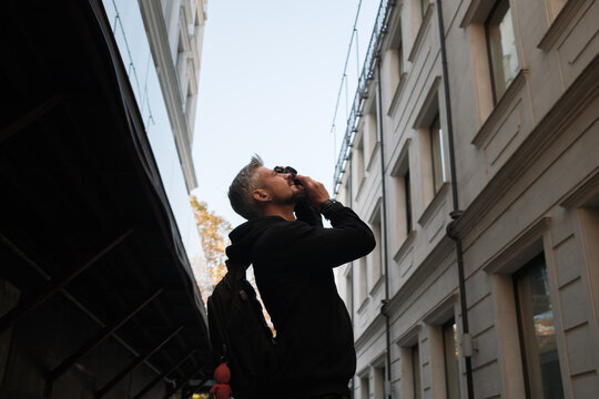 A person gazing upwards beside urban buildings, evoking curiosity and exploration. - Powered by Adobe