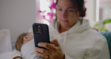 Close-up of a mother using her phone while her baby rests on her lap in a peaceful living room...