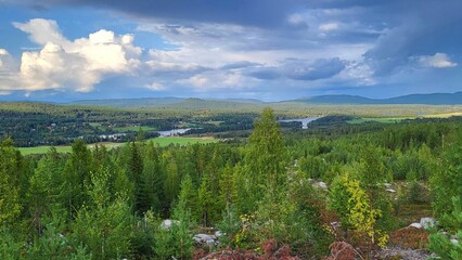 A breathtaking landscape showcases dense forests and rolling hills beneath a colorful sky filled...