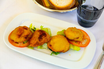 Potatoes stuffed with meat are laid out on pillow of vegetables. On snow-white plate, on top of layer of sliced goods and lettuce leaves, there are potatoes stuffed with meat