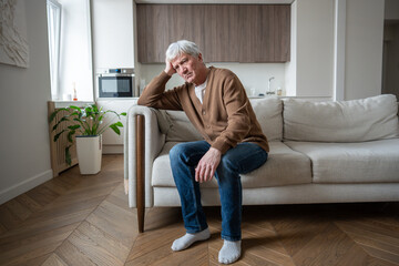 Lonely senior sits motionless supporting heavy head with hand showing advanced depression symptoms. Social isolation, cognitive decline, chronic headache, emotional numbness, neurodegenerative disease