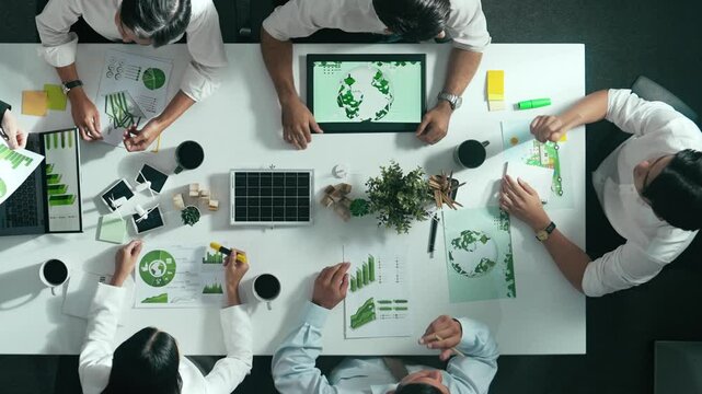 Top down view of business team discussing about using clean energy and sustainable investment at meeting table with wind mill, document with environmental graph and wooden house model. Alimentation.