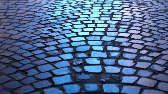 Wet cobblestone street reflecting blue light at night. Wet cobblestone street reflecting deep blue nighttime illumination, generating moody urban atmosphere with shimmering pavement texture